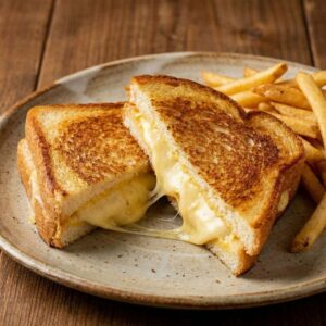 A gourmet grilled cheese sandwich cut in half with melted cheese stretching, served with french fries.