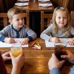 Two young children contentedly coloring at a wooden table in a family restaurant.