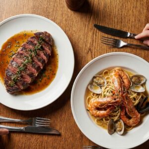 A spread of sliced steak and seafood pasta entrees ready for family-style sharing.